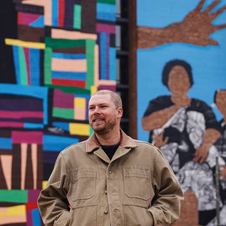 Atlanta-based artist Chastain “Chaz” Clark stands in front of his mural at Legacy at East Lake on Friday, Dec. 5, 2025. Clark completed the 80-foot mural on the side of the senior affordable housing high-rise in 2025. (Natrice Miller/AJC)