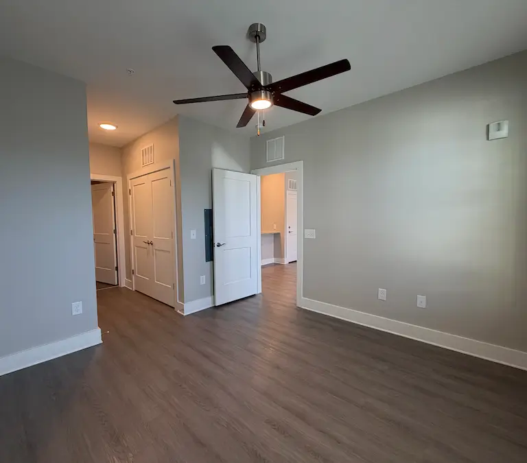 Spacious apartment bedroom with ceiling fan and connected living area