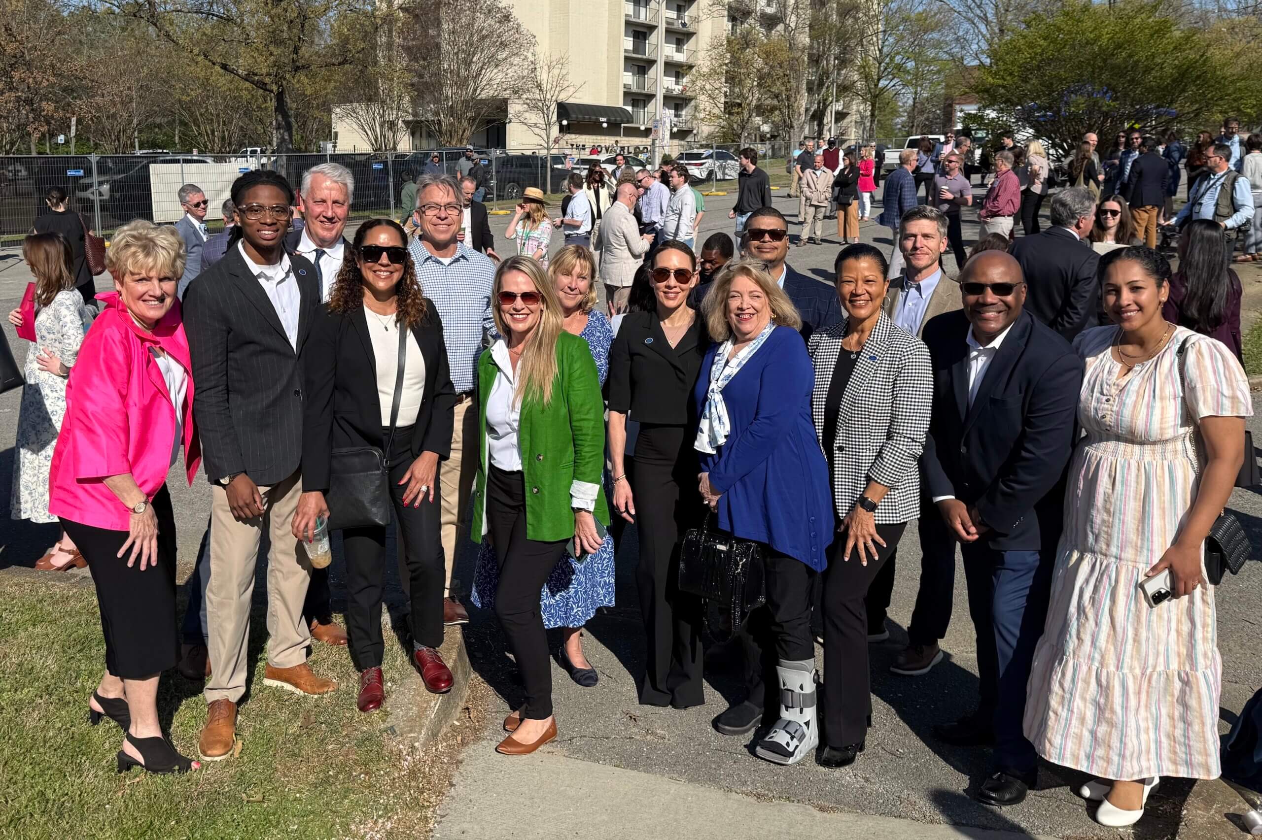 At the groundbreaking for Phase 2 of One Westside, a group of people standing outside, smiling at the camera. Trees, building, and a construction fence are visible in the background.