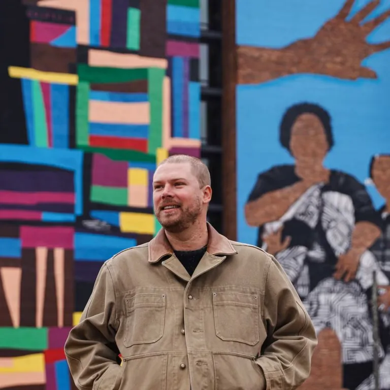 Atlanta-based artist Chastain “Chaz” Clark stands in front of his mural at Legacy at East Lake on Friday, Dec. 5, 2025. Clark completed the 80-foot mural on the side of the senior affordable housing high-rise in 2025. (Natrice Miller/AJC)